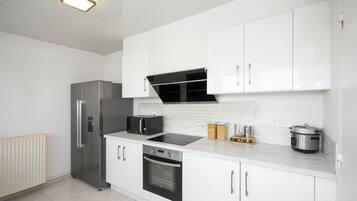 Een moderne keuken met witte kasten, een inbouwoven, een magnetron en een roestvrijstalen koelkast.