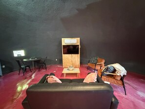 A room with a black leather sofa, a small wooden table, a television mounted on a wooden panel, and a red carpeted floor. - Purple Dome : One of Kind Geodesic Dome for two (Van Alstyne)