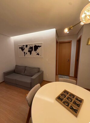 Ein Wohnzimmer mit einem grauen Sofa, einem runden Tisch mit Holzwürfeln, die 'GOOD LUCK' buchstabieren, und zwei Weltkarten an der Wand.