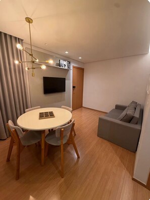 A modern living room with a round dining table, grey sofa, and a mounted TV.