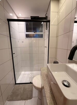 A modern bathroom with a glass shower enclosure, a toilet, and a sink with a faucet. - Fully furnished apartment near Lagoa Central and Confins. (Lagoa Santa)