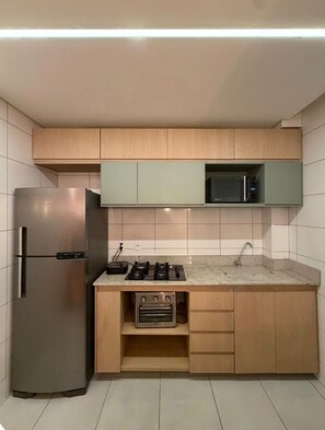 A compact kitchen with a stainless steel refrigerator, a microwave, a gas stove, and wooden cabinets. - Fully furnished apartment near Lagoa Central and Confins. (Lagoa Santa)