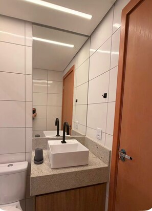 Ein Badezimmer mit weiß gefliesten Wänden, einer Holztür und einem Waschbecken mit Spiegel auf der Ablagefläche.