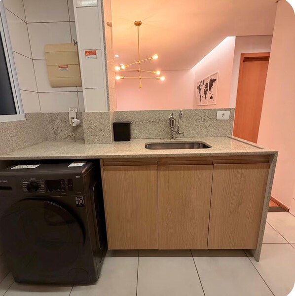 A compact kitchen with a built-in washing machine, a sink, and a modern chandelier.