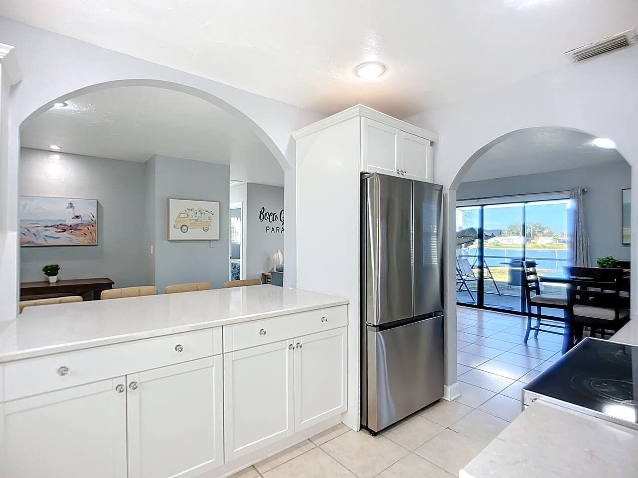 Una cocina moderna con armarios blancos, un refrigerador de acero inoxidable y un comedor con vistas al exterior.