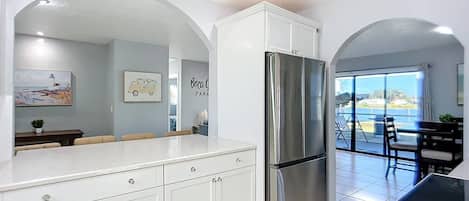 Una cocina moderna con armarios blancos, un refrigerador de acero inoxidable y un comedor con vistas al exterior.