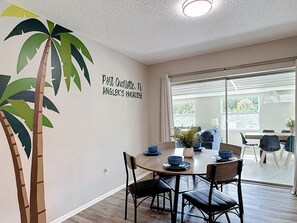 A dining area with a table set for four, a wall-mounted plant, and a sign reading 'Port Charlotte, FL ANGEL'S PARADISE.' - 5-Bed Coastal Retreat & Hot Tub (Port Charlotte)