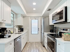 A compact kitchen with white cabinetry, a built-in microwave, a stove, and a dishwasher. - 5-Bed Coastal Retreat & Hot Tub (Port Charlotte)