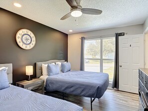 Ein Schlafzimmer mit zwei Betten, einem Deckenventilator, einer Wanduhr und einer Schiebetür nach draußen.