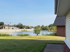 A view of a grassy area with a body of water, a brick building, and a clear sky.