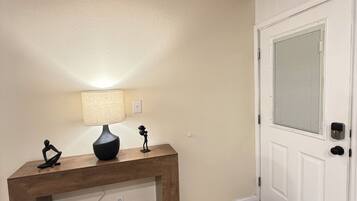 A wooden console table with a lamp and figurines, a white door with a window, and a tiled floor.