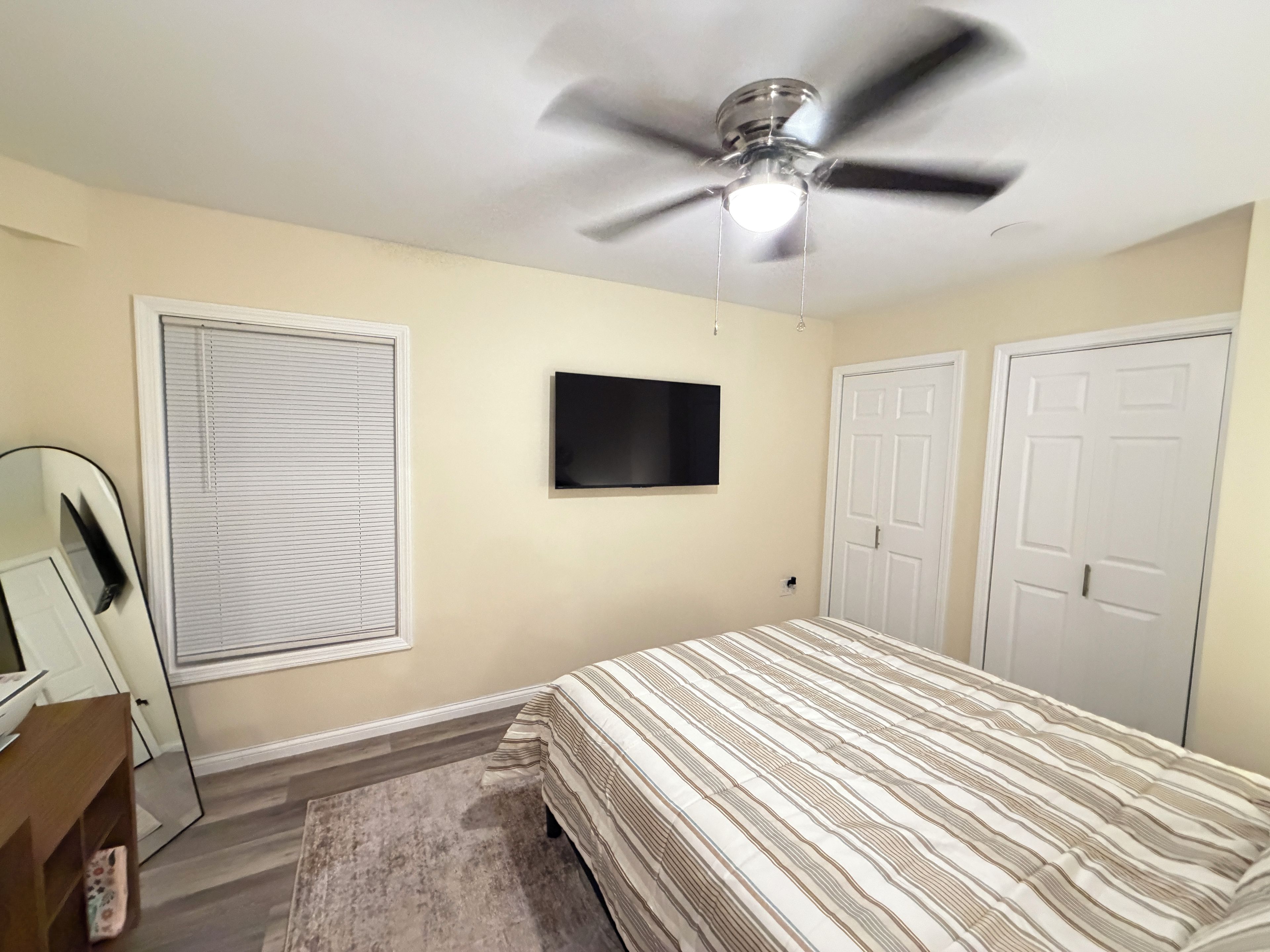 A bedroom with a bed, a ceiling fan, a television, and a door.