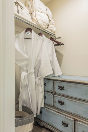 Ein weißer Bademantel hängt an einem Holzaufhänger, ein weißer Korb und eine blaue Kommode mit Schubladen.