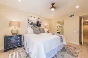 A bedroom with a large bed, two bedside tables, a floor lamp, and a painting on the wall. - Casa Allure - A Ryson Property (Palm Springs)