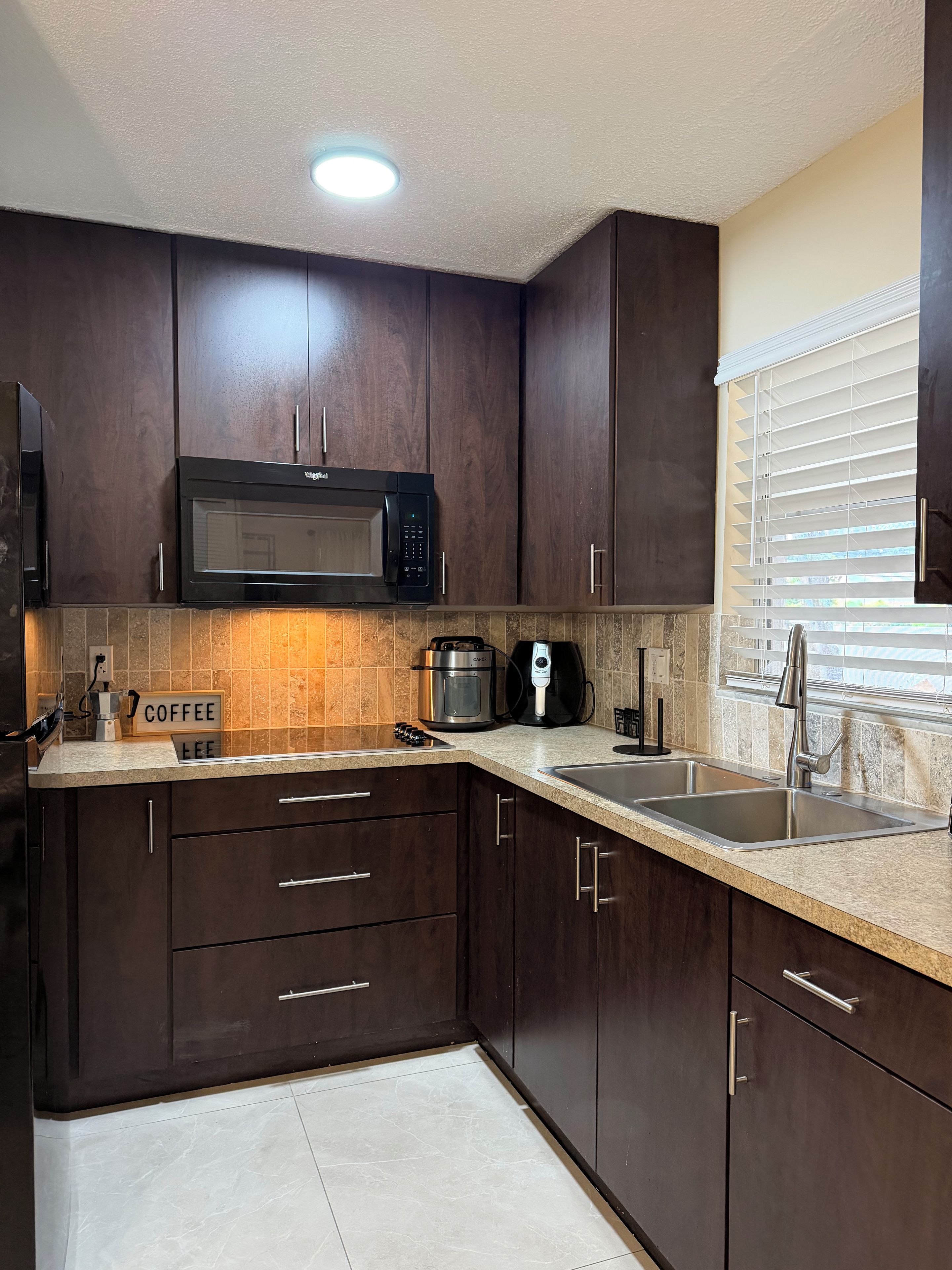 A modern kitchen with dark wooden cabinets, a built-in microwave, a coffee maker, and a sink.