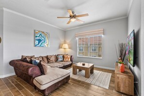 A living room with a sectional sofa, a coffee table, a ceiling fan, a TV, and artwork on the walls. - Vista Cay at Epic Universe : Luxury Lake view 4 bedroom condo (Orlando)