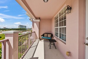 A balcony with a cushioned seating area, a small table, and a window with blinds. - Vista Cay at Epic Universe : Luxury Lake view 4 bedroom condo (Orlando)