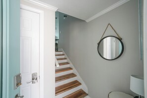 Un escalier en bois menant à un palier, une porte blanche dotée d’un clavier pour l’ouverture, et un miroir fixé au mur.
