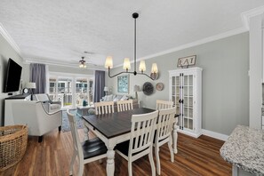 A dining area with a dark wooden table, white chairs, and a chandelier. - Brand New Listing, Beach, Pool, 2 K Beds (Mexico Beach)