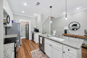 Une cuisine moderne avec des meubles blancs, des comptoirs en granit, des appareils électroménagers en acier inoxydable et un plancher en bois.