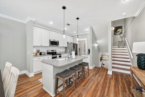 A modern kitchen with white cabinets, a granite countertop, and a central island with bar stools. - Brand New Listing, Beach, Pool, 2 K Beds (Mexico Beach)