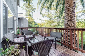 Une terrasse en bois avec des meubles en osier, un palmier et un mur en pierre.