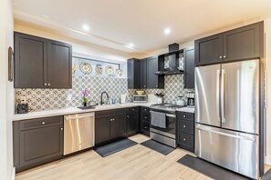 Une cuisine moderne avec des meubles de couleur sombre, des appareils en acier inoxydable et des carreaux décoratifs sur le mur derrière l’évier ou la cuisinière.