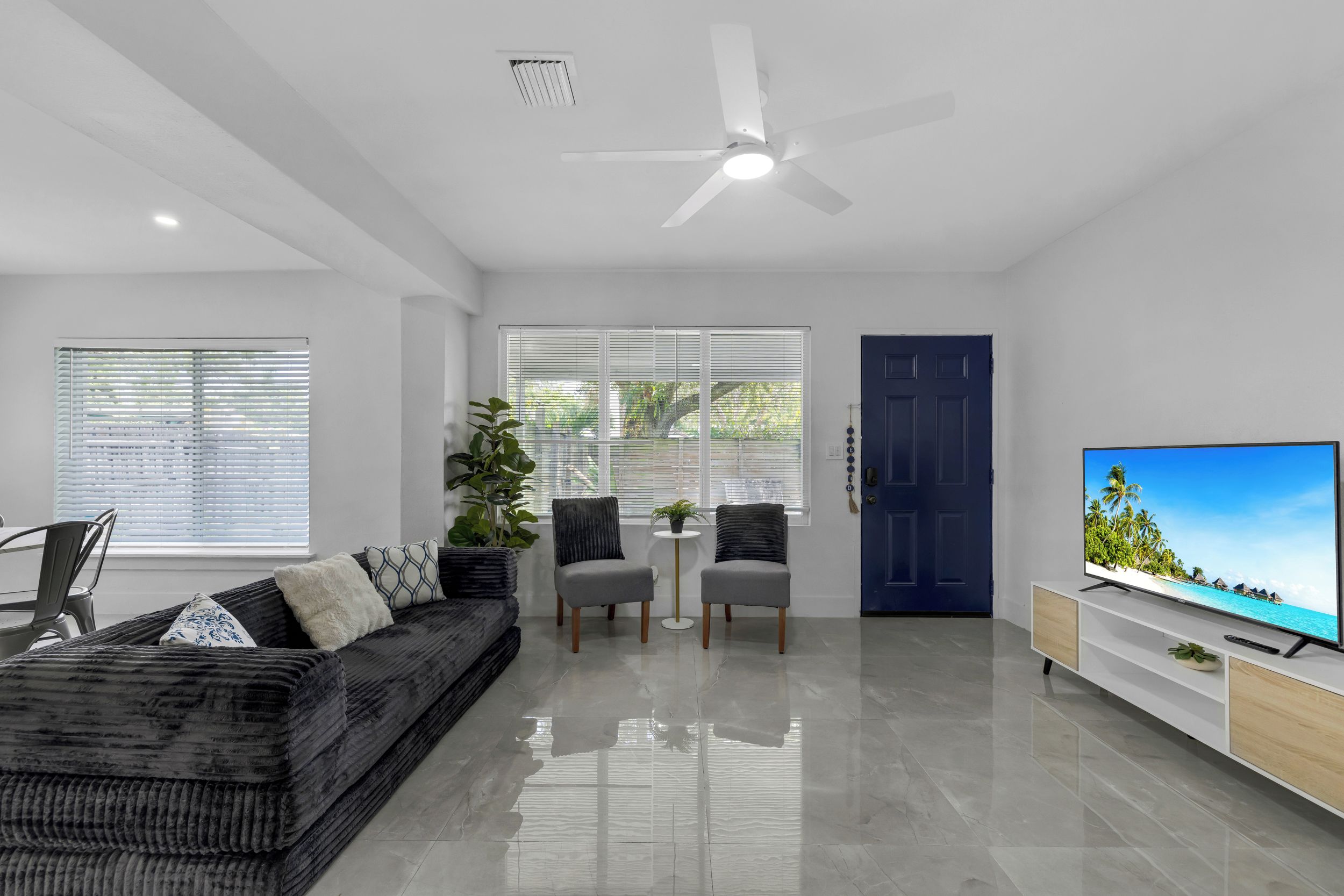 Una sala de estar moderna con un sofá, dos sillones, un televisor y un ventilador de techo.