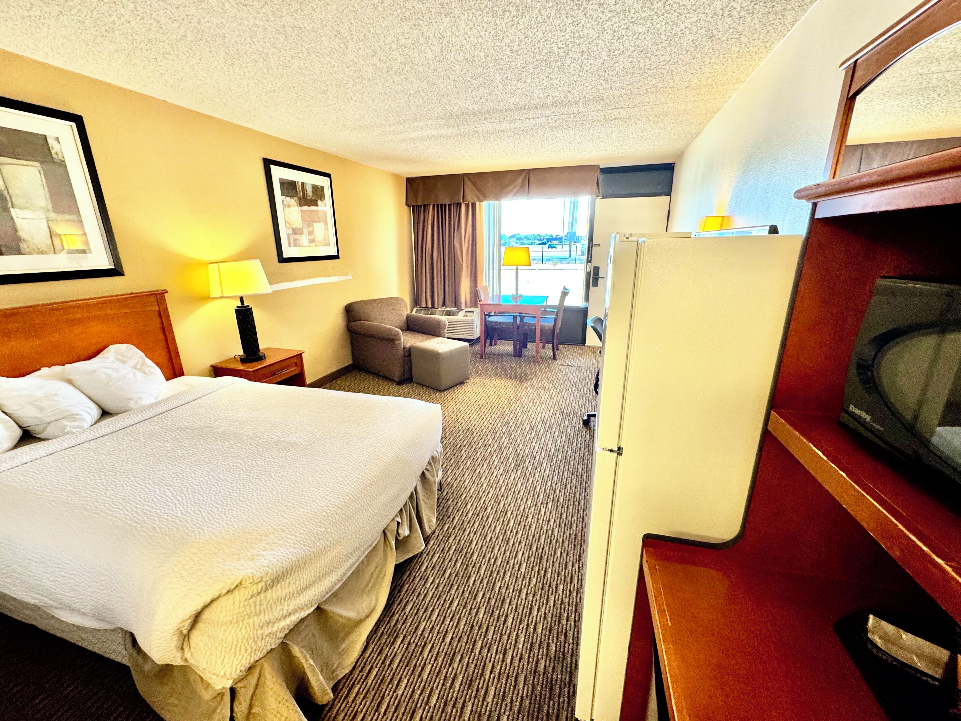 Ett hotellrum med en säng, ett skrivbord, en stol, en tv och ett fönster med gardiner.