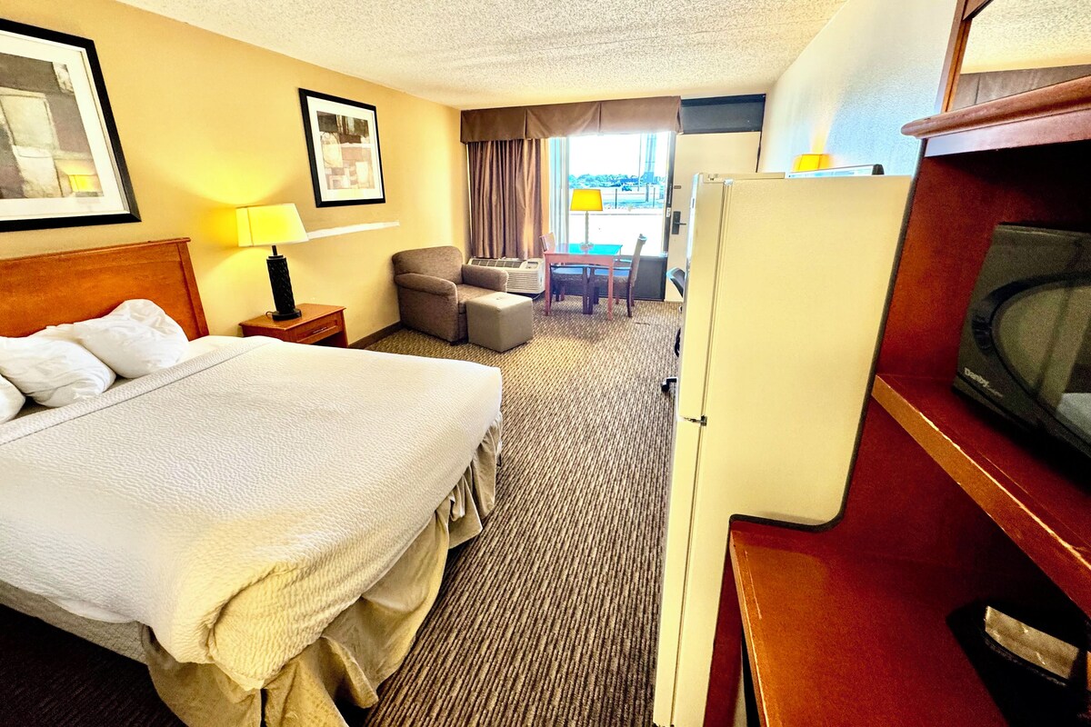 Ett hotellrum med en säng, ett skrivbord, en stol, en tv och ett fönster med gardiner.