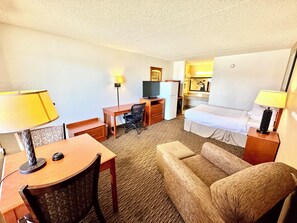 Ett hotellrum med en säng, ett skrivbord, en stol, en tv och ett litet pentry.