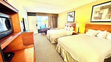 Ett hotellrum med två sängar, ett skrivbord, en stol, en tv och ett fönster med gardiner.