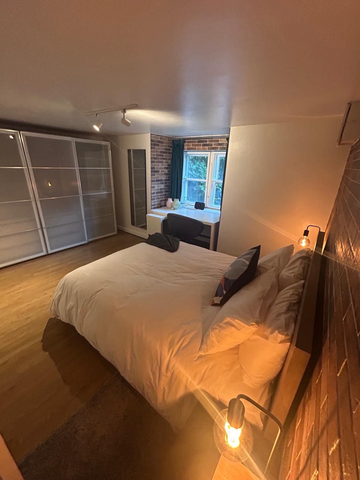 A bedroom with a bed, a desk, and a window.