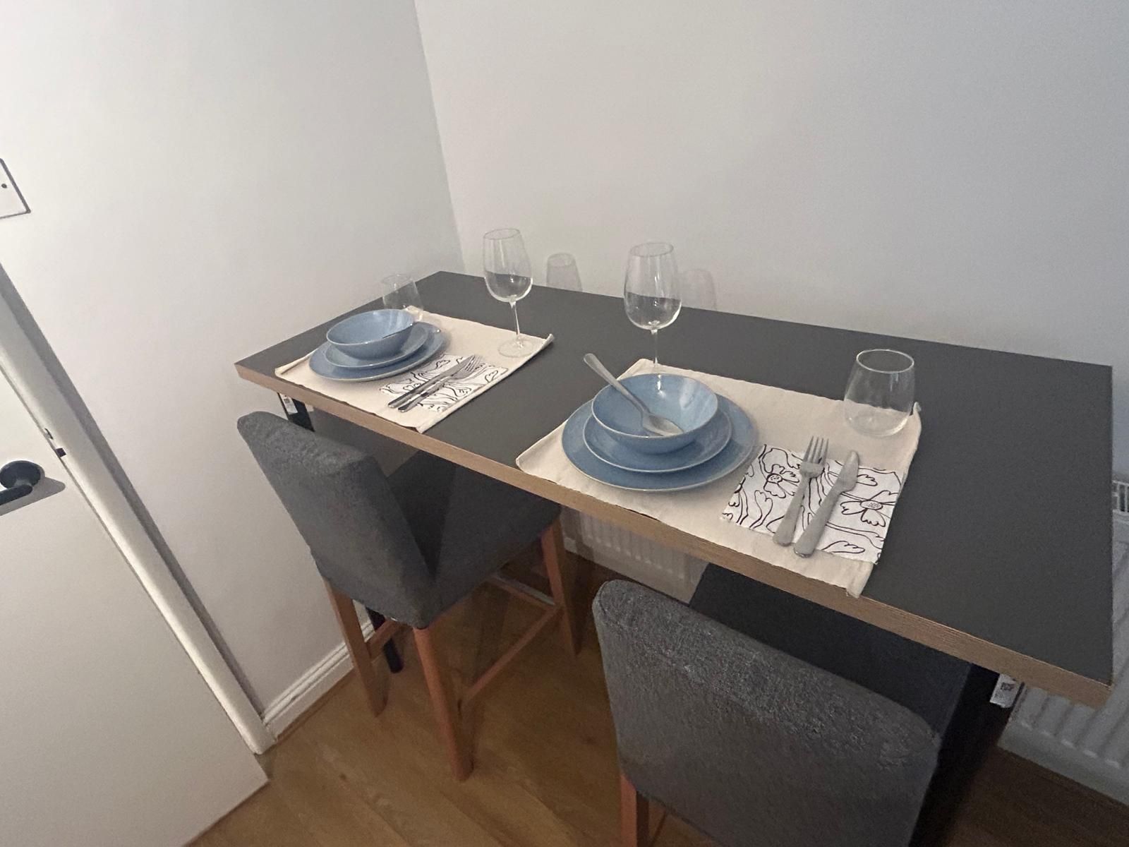 Een eettafel met twee stoelen, blauwe borden, bestek en wijnglazen.