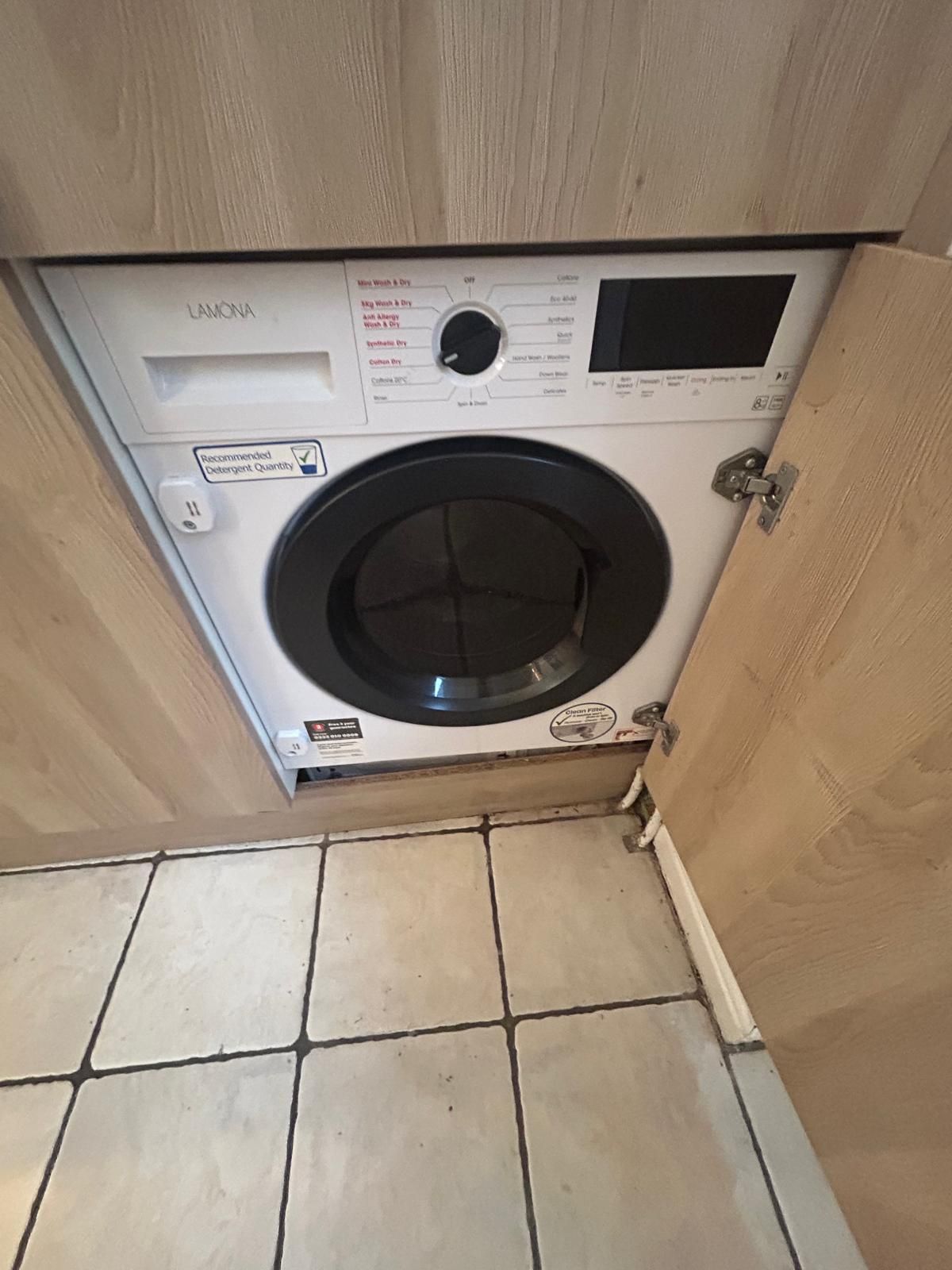 Vista frontal de una lavadora con panel de control, etiqueta indicando la cantidad recomendada de detergente y cable de alimentación.