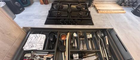 A kitchen with a stove, pots, and a drawer with utensils.