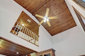 Une pièce avec un plafond en pente, un escalier en bois et un ventilateur de plafond.