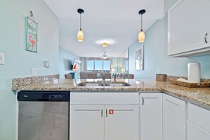 A kitchen with granite countertops, white cabinets, a dishwasher, and pendant lighting. - Gulf Front | Pool | Walk to Gulf Shores Favorites | BEACHBALL PROPERTIES (Gulf Shores)