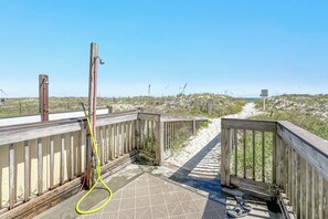 Een houten terras met een metalen hekwerk, een tuinslang en uitzicht op het strand.