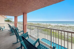 A balcony with green chairs and a pool, overlooking a beach with people and a clear sky. - Buena Vista 201 - Gulf-Front 3BR, Balcony Over the Pool - Beachball Properties (Gulf Shores)