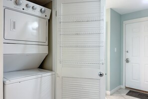 A laundry room with stacked washers and dryers, a metal drying rack, and a white door. - Gulf Front | Pool | Walk to Gulf Shores Favorites | BEACHBALL PROPERTIES (Gulf Shores)