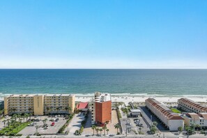 A coastal hotel with multiple buildings, a parking lot, and a beach in the background. - Buena Vista 201 - Gulf-Front 3BR, Balcony Over the Pool - Beachball Properties (Gulf Shores)