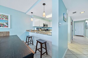 A kitchen with white cabinets, a microwave, and a sink. There are two wooden stools and a table. - Gulf Front | Pool | Walk to Gulf Shores Favorites | BEACHBALL PROPERTIES (Gulf Shores)