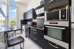 A compact kitchen with a washing machine, a microwave, and an oven. - Appartement Bleu Panorama - Welkeys (Bandol)