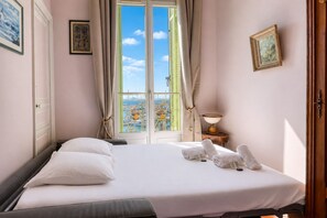 A hotel room with a bed, a view of the sea, and a window with curtains. - Appartement Bleu Panorama - Welkeys (Bandol)