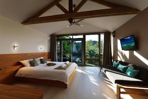Un dormitorio con una cama grande, un sofá, un televisor y un balcón con vistas a la vegetación.