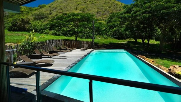 Piscina com espreguiçadeiras e vista para uma colina verde.