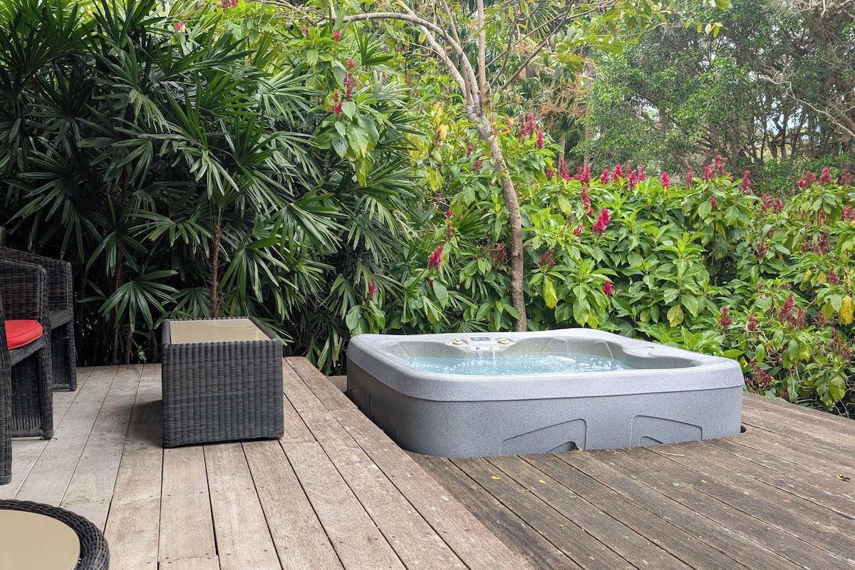 Un patio al aire libre con mobiliario de mimbre, un jacuzzi y abundante vegetación.