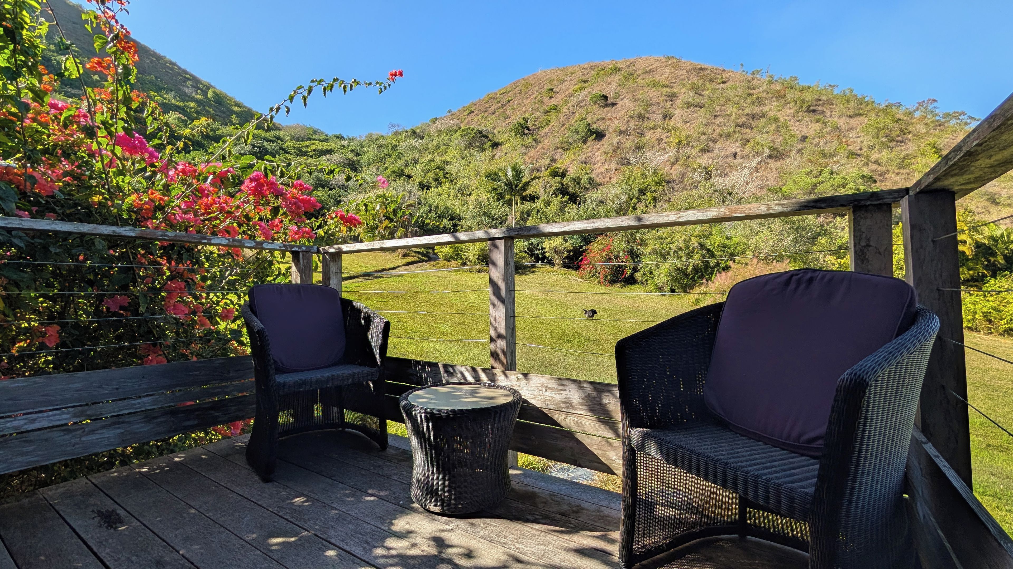 An outdoor patio with wicker furniture and a view of a hilly landscape.