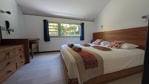 A bedroom with a wooden headboard, a large bed with multiple pillows, a bedside table, and a window with curtains.